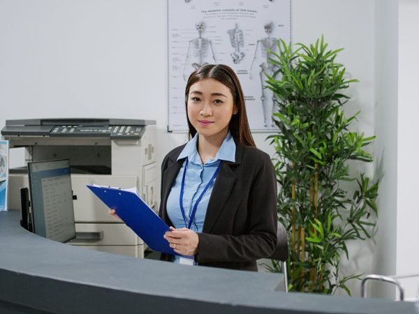 Portrait of asian receptionist working with medical checkup papers and appointment reports at facility registration desk. Clinic staff at hospital reception counter. Handheld shot. SSUCv3H4sIAAAAAAAACnRSTWvcMBD9K0bn1VaSJcvaW2mThkIgFHrKhjKSxrGJ1zK2nFJC/ntHTkJPvc3Hmzea9/TCPKxDYKcXNozjtuYF8pAmdhIHtuAUcdnD56VuxB5hHHJaBhj3zEMO/QQXZKdpG8fXA1sz5G3FlRgpC5DxkeB7/rHq/qXU2YndIIy5D7Dgp1viDURKBJun1u2wBhxHmDBtK3s9fIzcYZpH/B/s4cDgEafwp2yn9QuOCPtj7plq21bVEbjqAnAtjeStkpFDq3VQPtTWBeJtReOUVYErE5DrxnsOEQUP3ksZlenQNQSD2gRjbMeFdY5gUXMHOnDRoZbKudpES7CoGkoc8mhkw7WWggOC5tJoETrlXWMLzET0SlFTKtlxHbTlHlFxFzpjgnWxITY67ul3xuXyri1scUhF1udEylGxpuK8DGGYHt8QKffFP9IubVNeSBUmraZ9Y0ozeNLx1NEkHlgP60qY+F4oztFfSJc3ninloiErB0GmKSbrWrjWaONIBOFqZYolu/X9QINlV5mkMDwN8f3FA/EzaKIKGB03wliuobW81bLmXfAhkje17oq/2zwmiLkcSJNdWi67/wusJMF+Ah09Q+6peHU6n+Wx+rmP0PXVXZ9yWs9nsuFYXV9VPzDgXP51dZ3osIpXN2mdhwzjv9ZO8TVNeD5/FnX9S1ihpKLgi7TtUUjRaqvF8fvdN/b6FwAA//8DAKM2uWc2AwAA